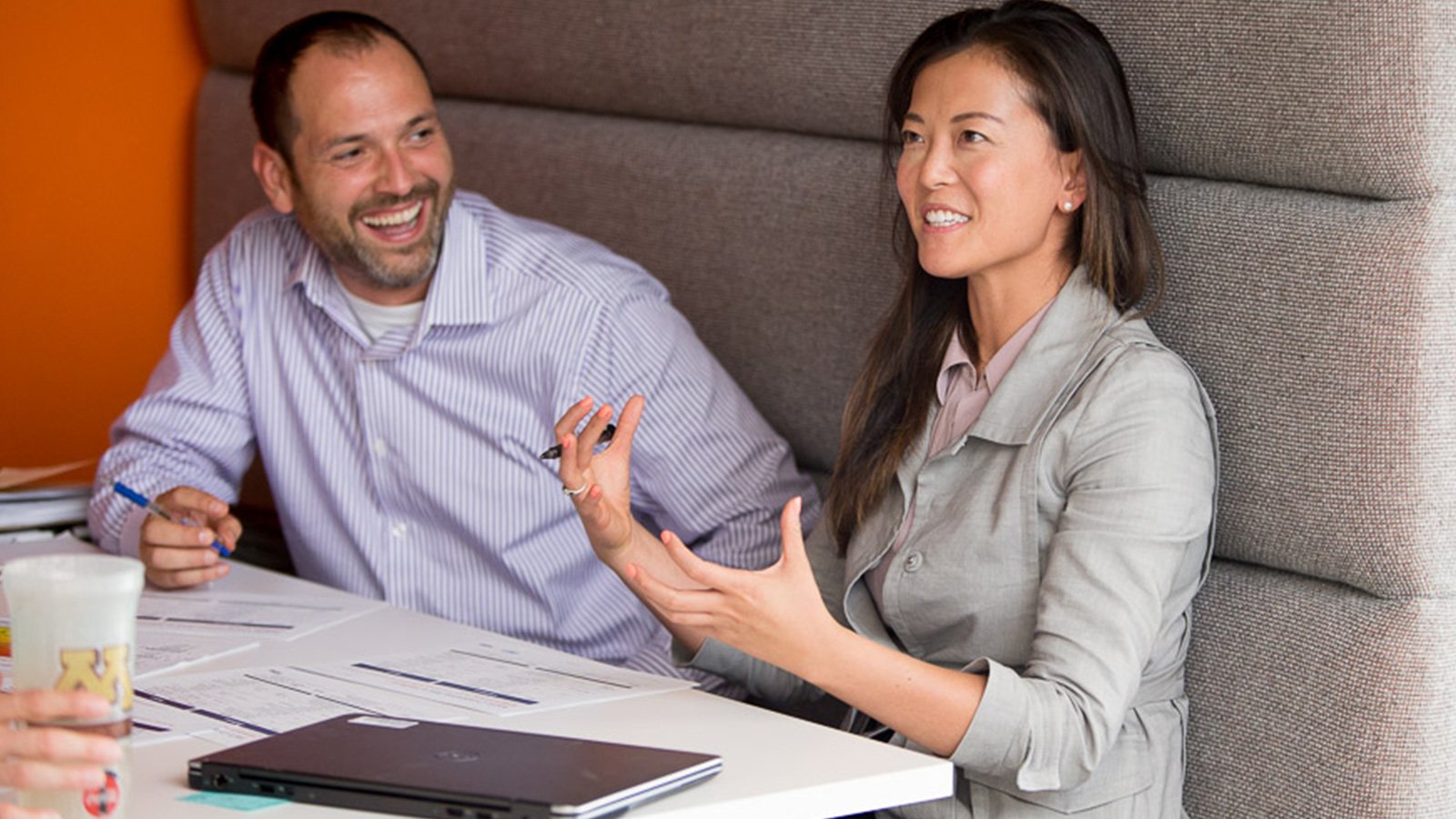 Man and woman at table with closed laptop discussing document.