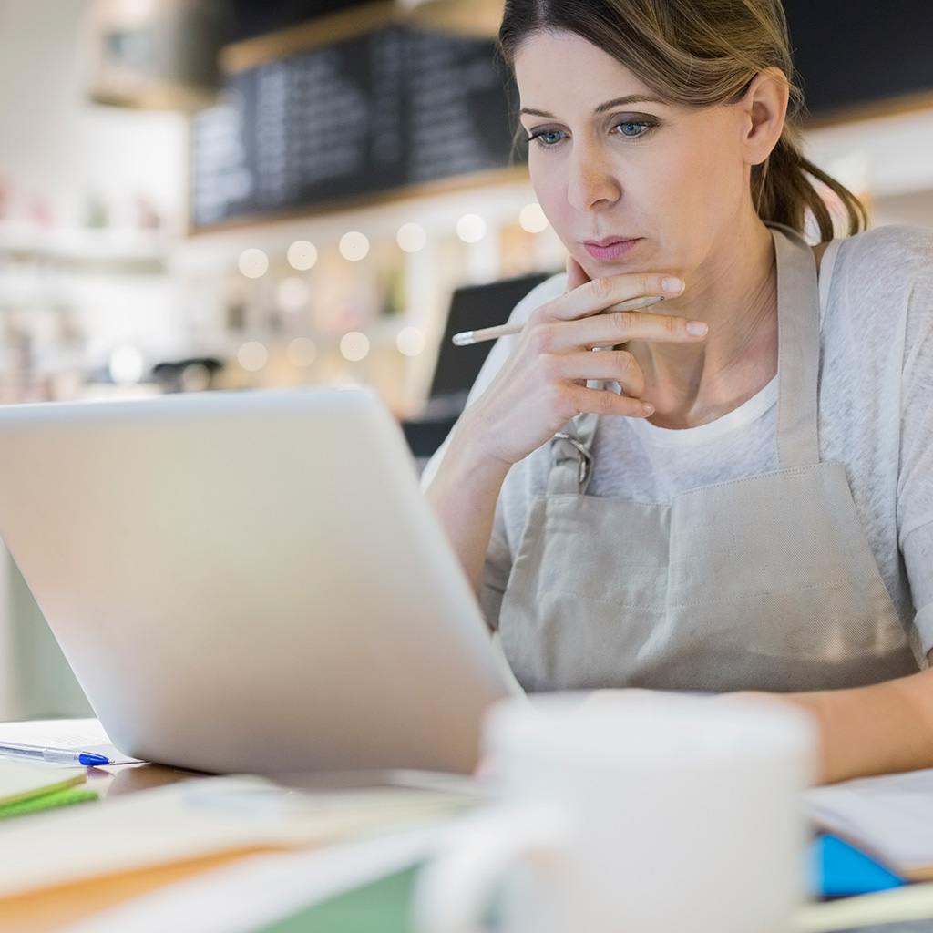 A woman sitting at a desk, looking pensive while staring at her laptop.