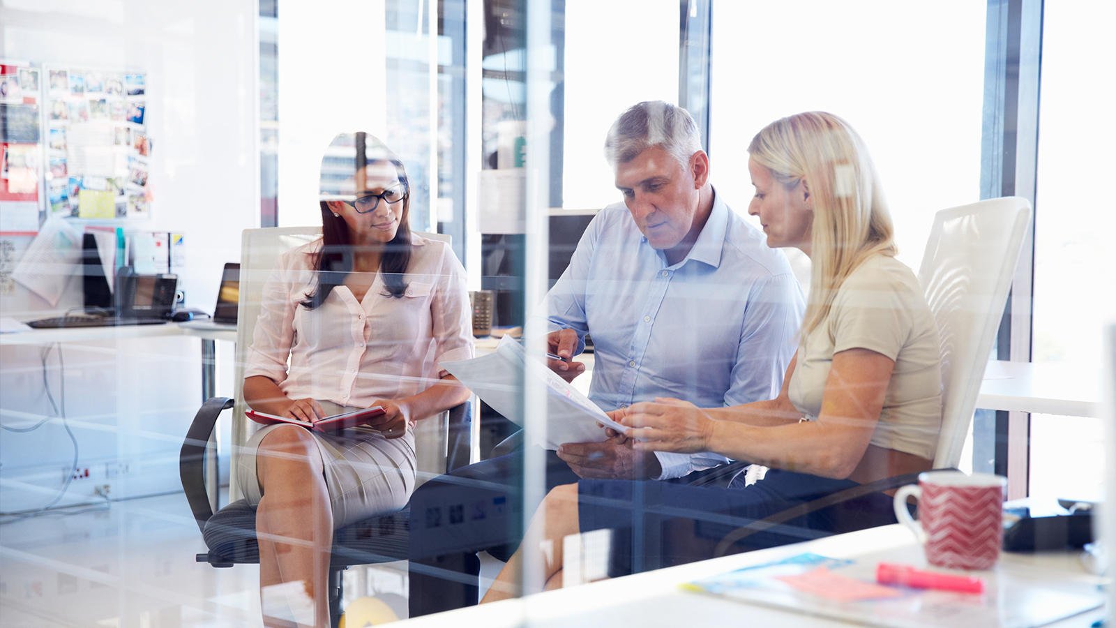 Three people seated in an office discussing work-related issues. Three people seated in an office discussing work-related issues.