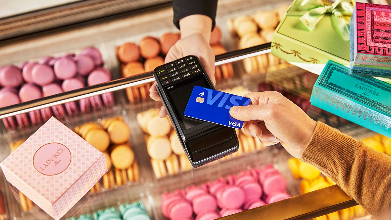 A person demonstrates contactless payments by holding a credit card in front of a display of cookies.
