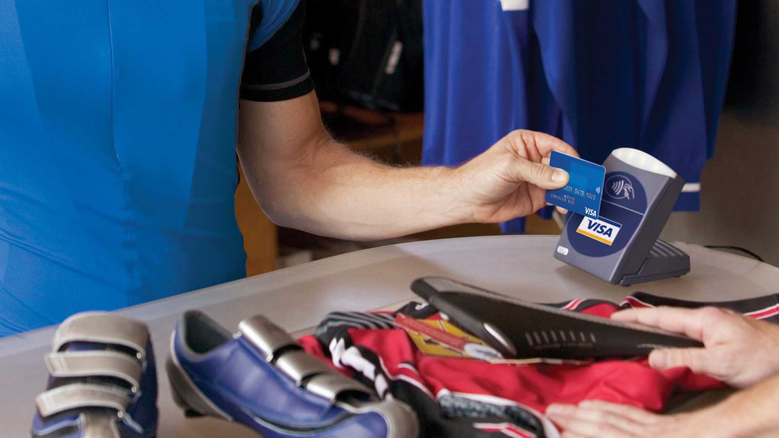 An individual completes a transaction for shoes at a small shop due to presence of a Visa system for contactless payment for merchants.