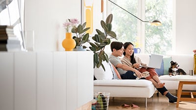 photo of a dog and two people using a laptop while sitting on a sofa and using the click to pay method for their online purchases.