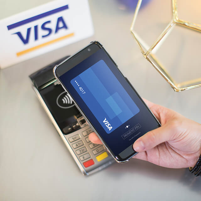A closeup of a shopper using the Visa card on her phone to make a contactless payment at a terminal.