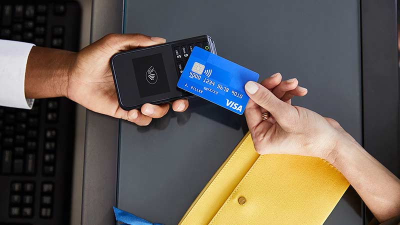 Hand holding a contactless credit card across a counter up to a contactless point of sale terminal being held by another hand